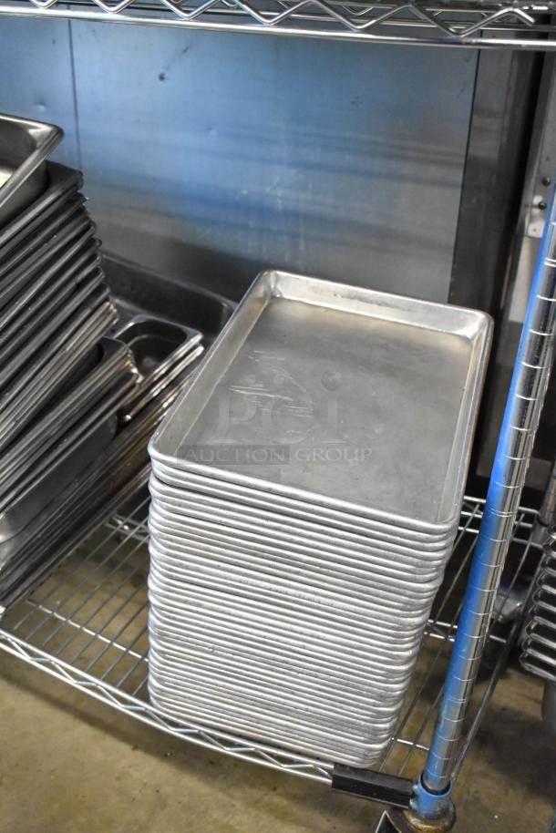 Stack of metal baking pans and stainless steel drop-in bins on shelving, in used condition.