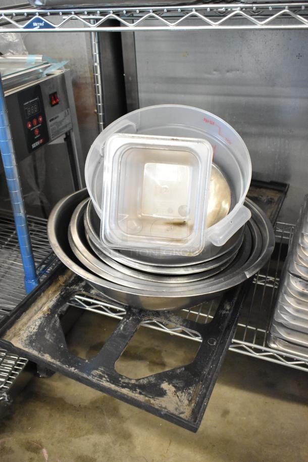 Assorted kitchenware lot with stainless steel drop-in bins, metal baking pans, and bowls, placed on metal shelving.