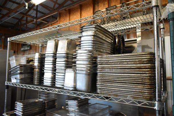 Metal shelves with stacked stainless steel and poly drop-in bins, and metal baking pans, showing signs of light use.