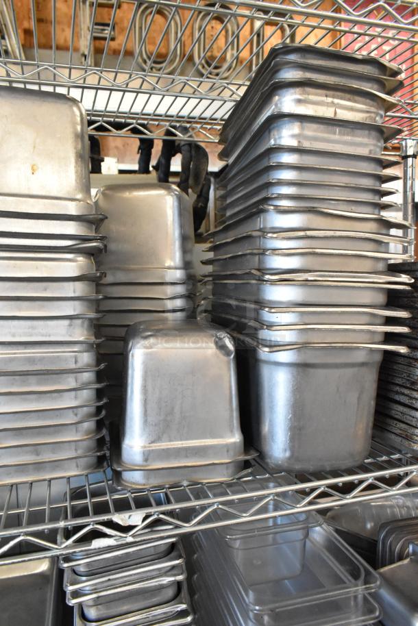 Stacked stainless steel drop-in bins and metal baking pans on a wire rack, showing slight wear, ready for auction.