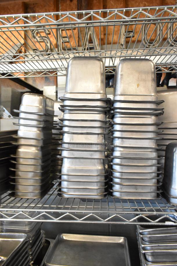 Tiered lot of stainless steel drop-in bins, metal baking pans, and poly drop-in bins, stacked on wire shelving.