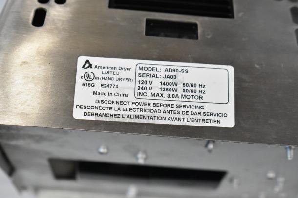 American Dryer AD90-SS label showing model, serial (JA03), voltage, and power specs; stainless steel cover visible.