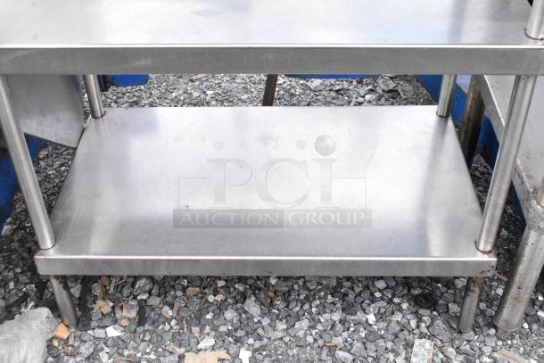 Stainless steel table with two under shelves, durable structure, shows minor signs of use, commercial-grade finish.