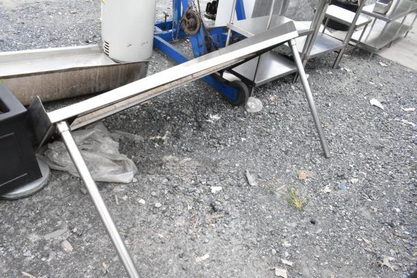 Stainless steel shelf with angled legs, showing minor signs of wear on gravel surface. Ideal for durable storage solutions.