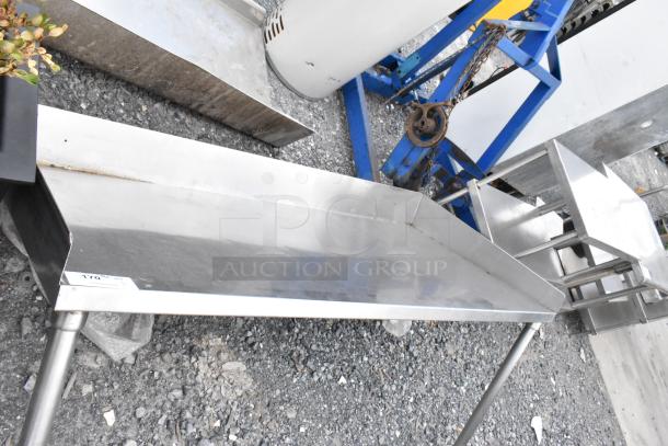 Stainless steel shelf with sturdy legs, slightly used condition, reflective surface, ideal for commercial use.