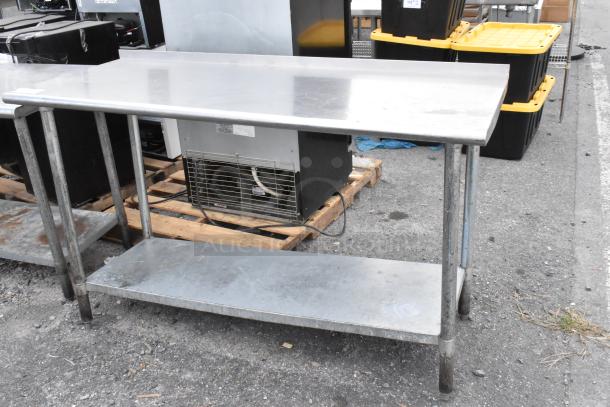 Stainless steel table with metal under shelf, shows wear. Ideal for industrial or kitchen use. No visible branding.