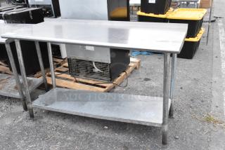 Stainless steel table with metal under shelf, shows wear. Ideal for industrial or kitchen use. No visible branding.