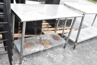Stainless steel table with metal under shelf, showing signs of rust and wear, sturdy construction for industrial use.