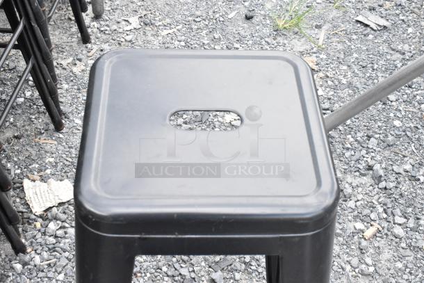 Black metal Tolix style bar stool with cutout handle on top, shown on gravel surface, part of a 38-piece auction lot.