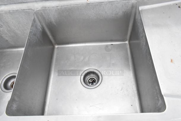 Stainless steel 3-bay sink with dual drain boards, durable and spacious. Visible scuff marks indicate moderate use.