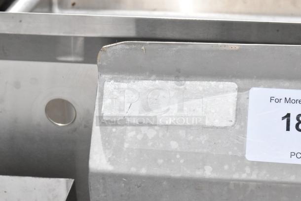 Stainless steel 3 bay sink with dual drain boards, featuring signs of wear and a visible label for identification.