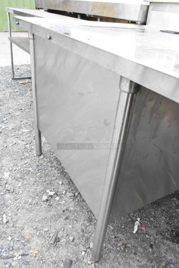 Stainless steel table with side under shelves, featuring a sturdy frame. Appears in used condition with minor surface wear.
