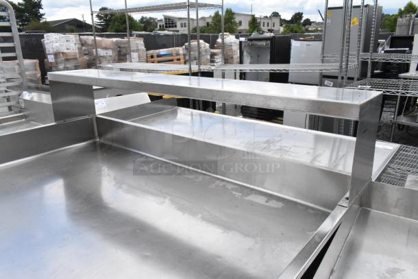 Stainless steel commercial table with elevated shelf, showing minor wear. Ideal for industrial kitchens.