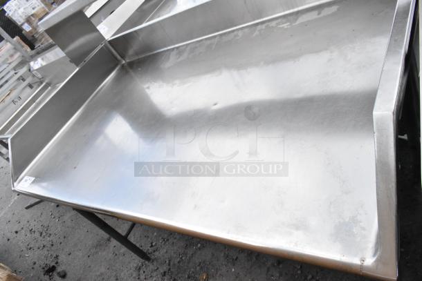 Stainless steel commercial table with back splash, used condition, visible surface wear, ideal for kitchens.