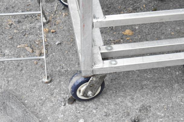 Metal commercial pan transport rack with sturdy casters, visible screws, and welded joints, showing minor wear.