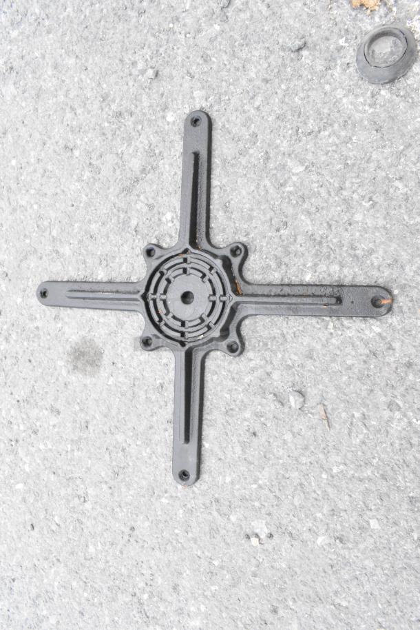 Industrial iron table leg cross base piece on concrete background, showing rust and wear.