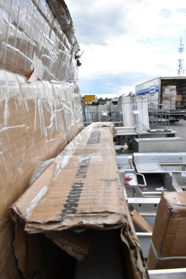Cardboard boxes containing sealed industrial kitchen equipment, labeled with Regency and Steelton branding. Boxes show visible wear.