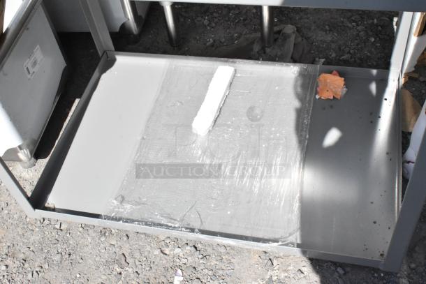 Gray metal 2-tier cart with commercial casters, new scratch and dent condition, wrapped in protective plastic on bottom shelf.