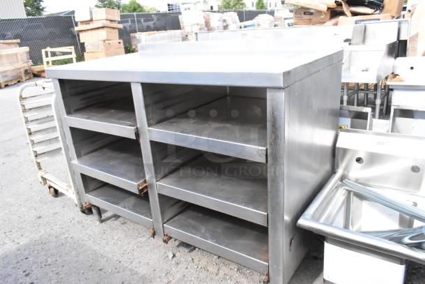 Stainless steel table with four under shelves, industrial-grade, durable design, used condition, suitable for kitchen or storage.