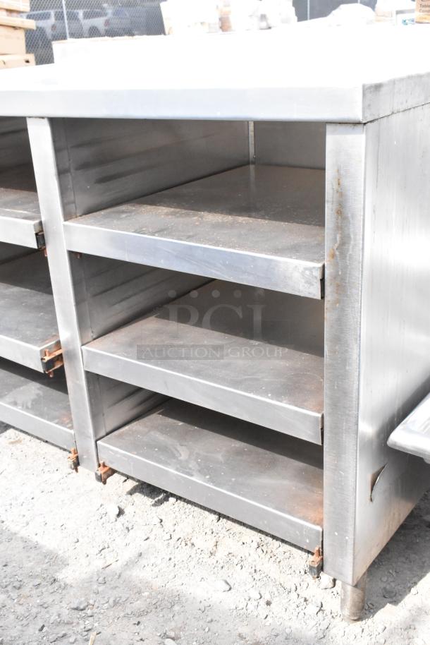 Stainless steel table with under shelves, showing signs of wear, ideal for kitchen or industrial use.