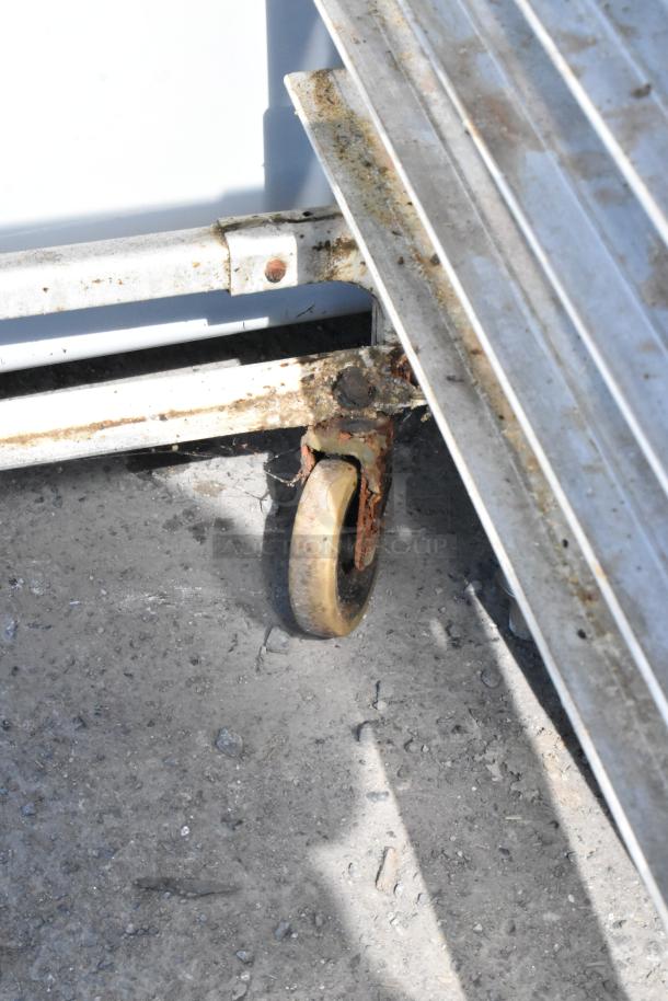 Metal pan transport rack with visible rust on commercial caster and frame. Suitable for heavy-duty kitchen use.