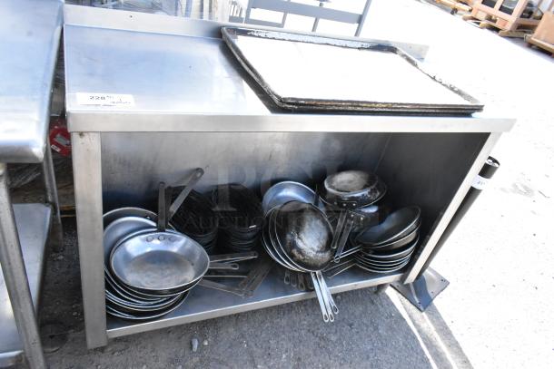Stainless steel table with under shelf, holding assorted skillets. Slight wear on surface, ideal for kitchen use.