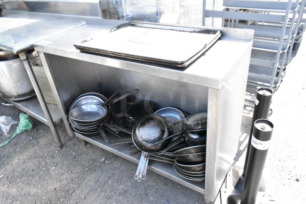 Stainless steel table with under shelf, filled with assorted skillets and trays. Well-used condition.