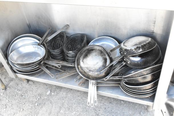 Stainless steel table with under shelf, containing multiple skillets and wire racks. Skillets show signs of use.
