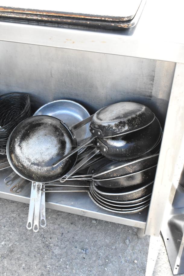 Stainless steel table with under shelf, includes stack of skillets. Signs of wear on skillets; table in good condition.