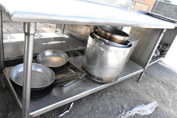 Stainless steel table with under shelf, includes skillets and stock pots. Visible wear on pots, table in good condition.