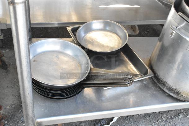 Stainless steel table with under shelf, includes skillets and stock pots, used condition, ideal for kitchen storage.