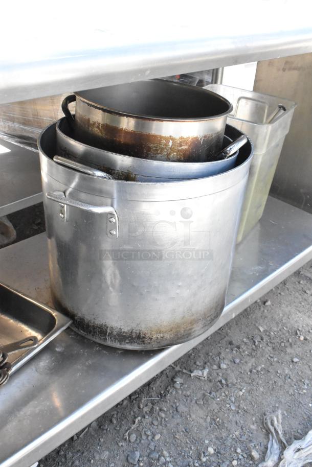 Stainless steel table with under shelf, containing skillets and stock pots, showing wear and in used condition.