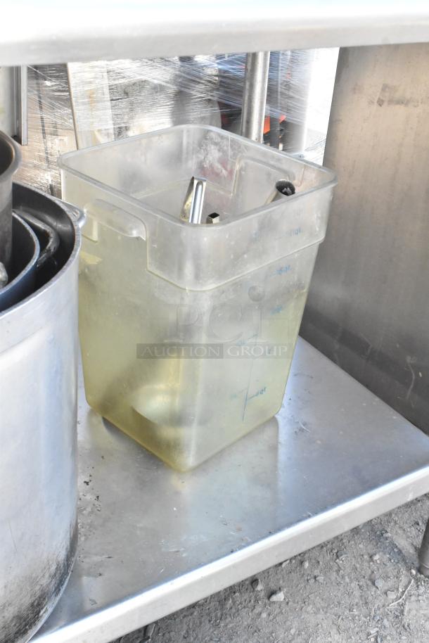 Stainless steel table with under shelf containing skillets, stock pots, and graduated storage container. Slightly worn condition.