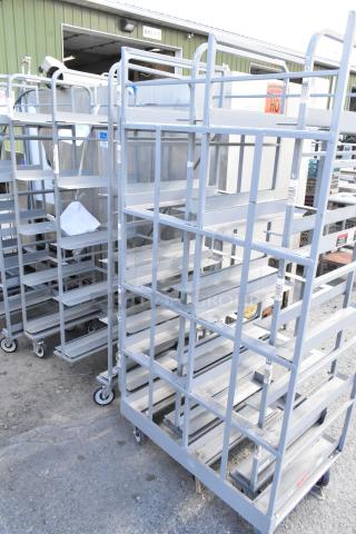 Two metal double transport racks on commercial casters, in used condition, showing sturdy construction and mobility features.