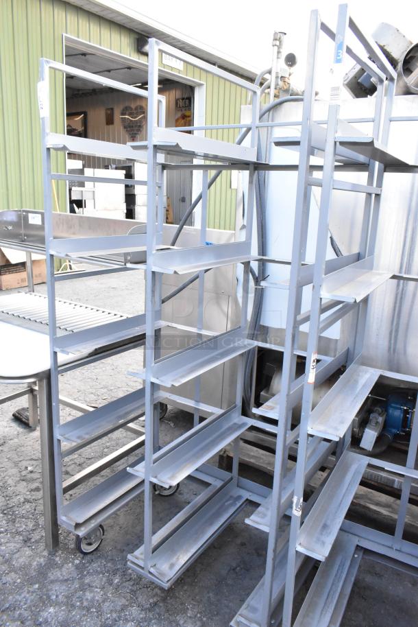 2 metal double transport racks on commercial casters, multi-tiered shelves, industrial condition, outdoor setting.