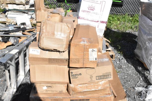 Boxes of new "scratch and dent" items, including stemless wine glasses and square mounts, on a gravel surface.