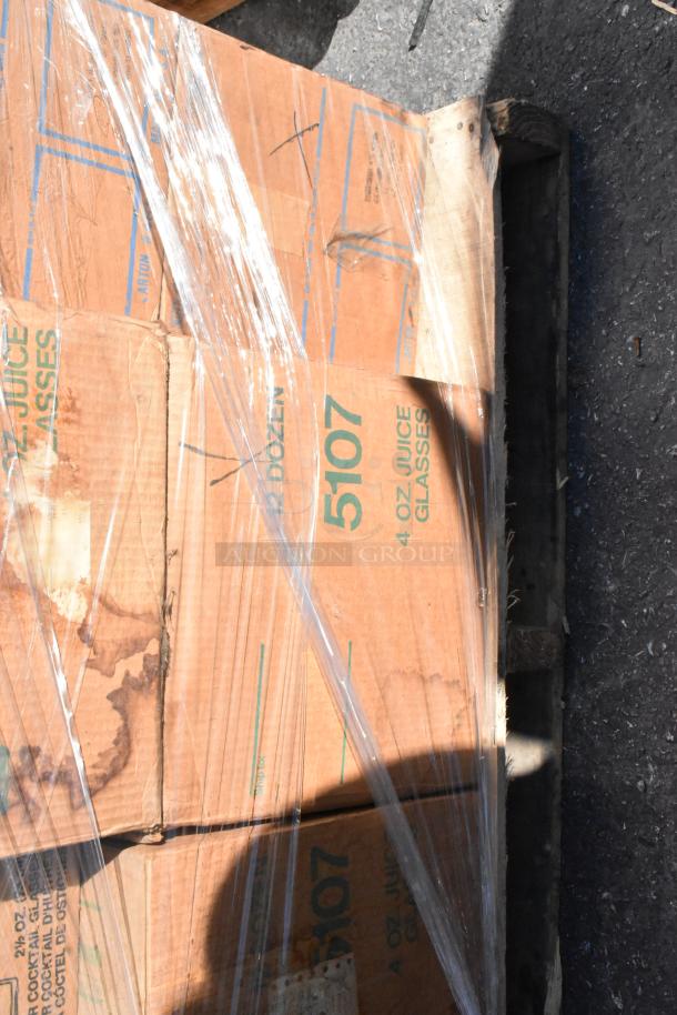 Sealed pallet of cardboard boxes labeled "4 oz. Juice Glasses" with visible wear and water stains.