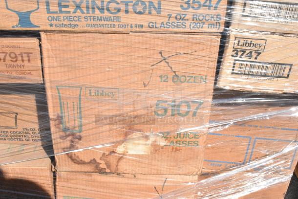 Stack of sealed boxes labeled Libbey glassware, including 7 oz rocks and juice glasses. Visible scratches and dents on boxes.