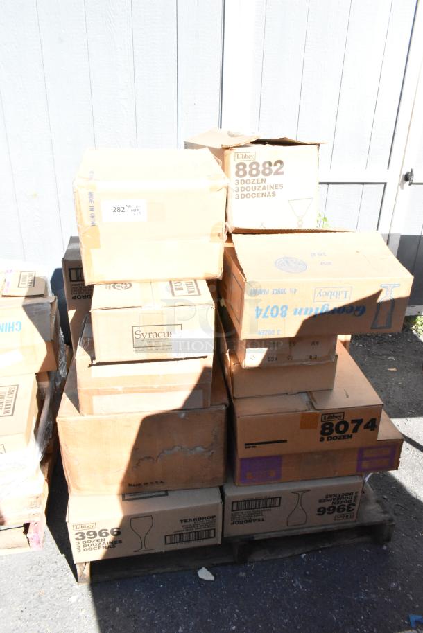 Stack of sealed boxes containing various brand new scratch and dent dishware items, including Libbey and Syracuse brands.