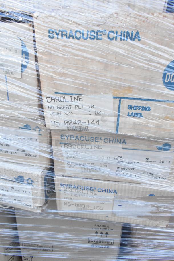 Stack of boxed Syracuse China dishware labeled "Caroline" and "Brookline," shrink-wrapped, indicating shipping labels and condition.