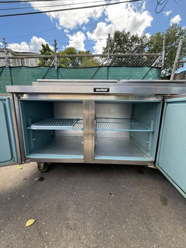 Delfield 18672BUCMP 72" undercounter refrigerator, stainless steel, open doors, interior shelving, outdoor setting.