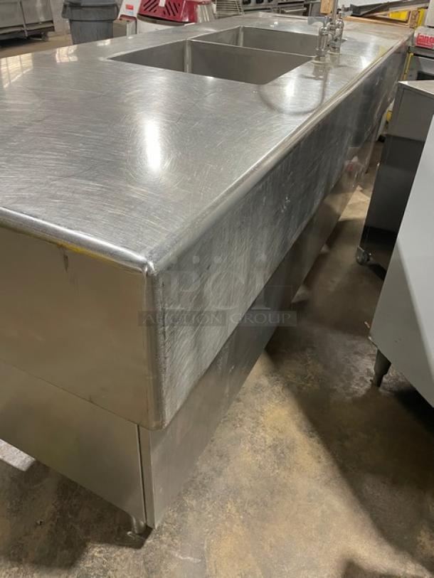 Custom stainless steel double compartment sink workstation with a gooseneck swivel faucet, enclosed cabinet base, and legs.