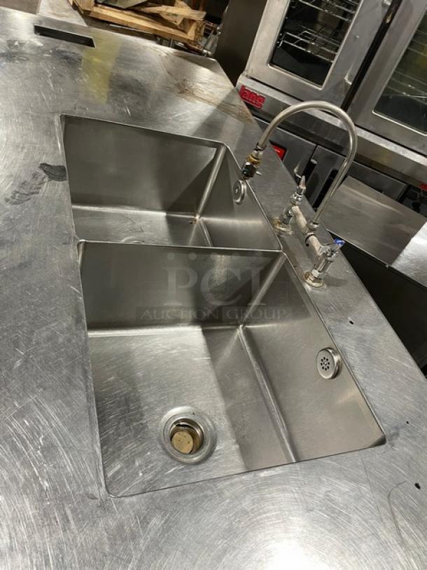 Custom stainless steel double compartment sink workstation with gooseneck swivel faucet and enclosed cabinet base on legs.