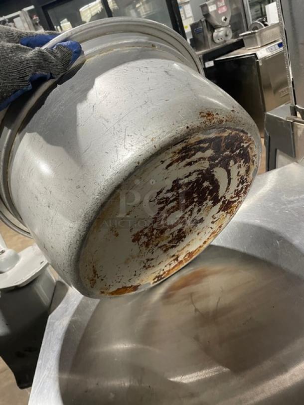Vintage commercial aluminum rice cooker with cover, showing visible wear and rust on the bottom, ideal for collectors.