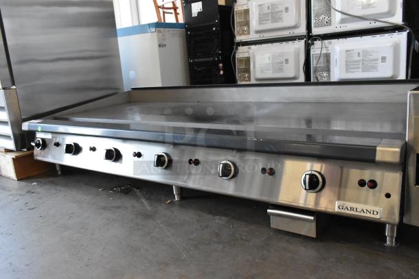 Garland Stainless Steel Commercial Flat Top Griddle, countertop design, multiple control knobs, industrial setting.