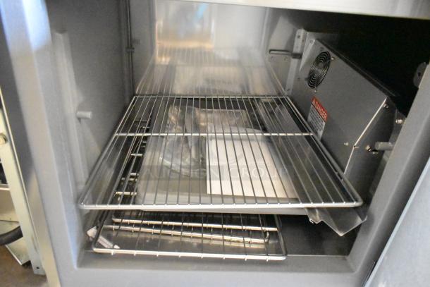 Delfield stainless steel commercial prep table interior, showing wire shelves and ventilation unit. 115V, 1-phase, commercial casters.