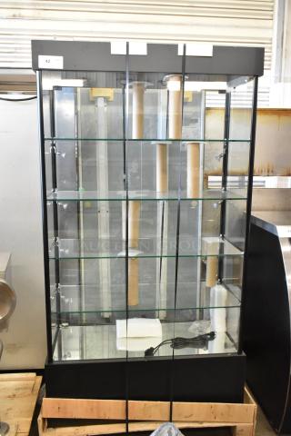 Brand new dry shelving unit display case with glass shelves, black frame, minor scratches, and electrical cord.