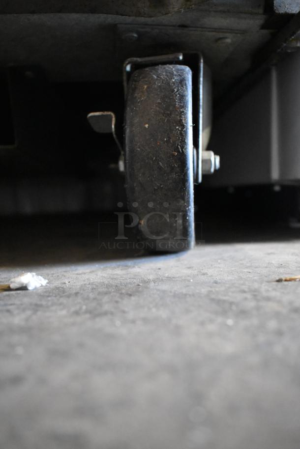 Commercial caster of a 2017 True TPP-67 stainless steel pizza prep table, showing wear, on a concrete floor.