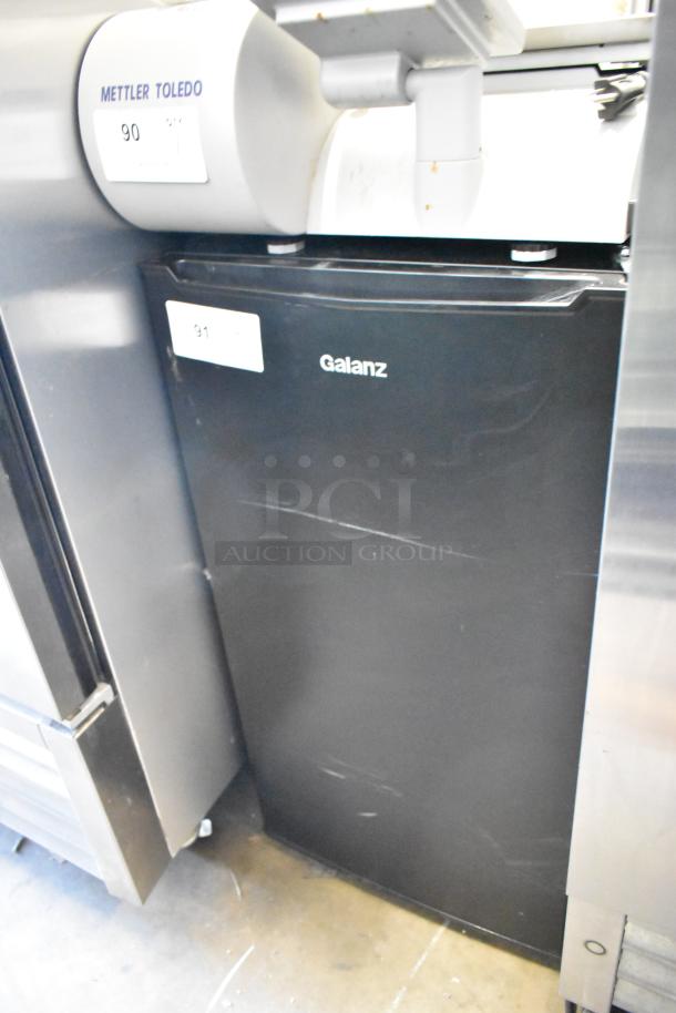 Galanz GLR33MBKE23 mini cooler, black, showing moderate wear, 115 volts, 1 phase, label indicates unit number 91.