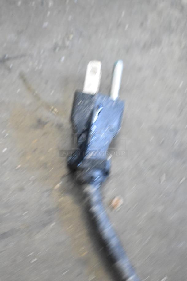 Blurred image of a power plug, possibly related to the Bunn CWTF15 coffee machine, on a concrete surface.